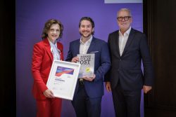 Die Ostbeauftragte der Bundesregierung, Elisabeth Kaiser mit dem CEO der Ucaneo GmbH, Florian Tiller und dem Präsidenten des Ostdeutschen Wirtschaftsforums, Frank Nehring. Kaiser zeigt eine Urkunde zur Preisverleihung. Neben ihr hält Tiller einen Sammelband „Denk ich an Ostdeutschland“ der Prima Vier Nehring Verlag GmbH in der Hand. Abbildung: Thomas Koehler